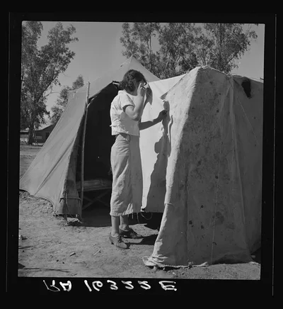 Woman in a California pea pickers' camp, mending the tent, 1937