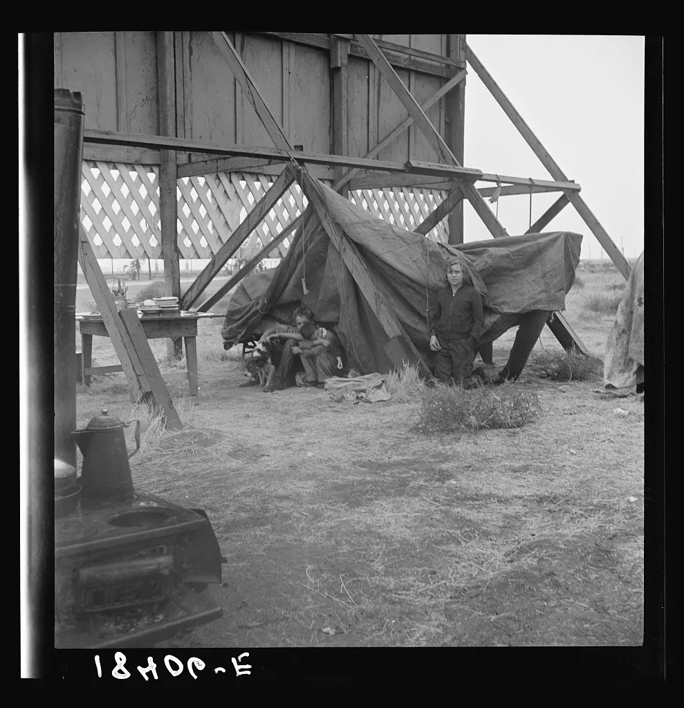 One of three families camped behind a billboard on U.S. 99. Kern…, California, 1938